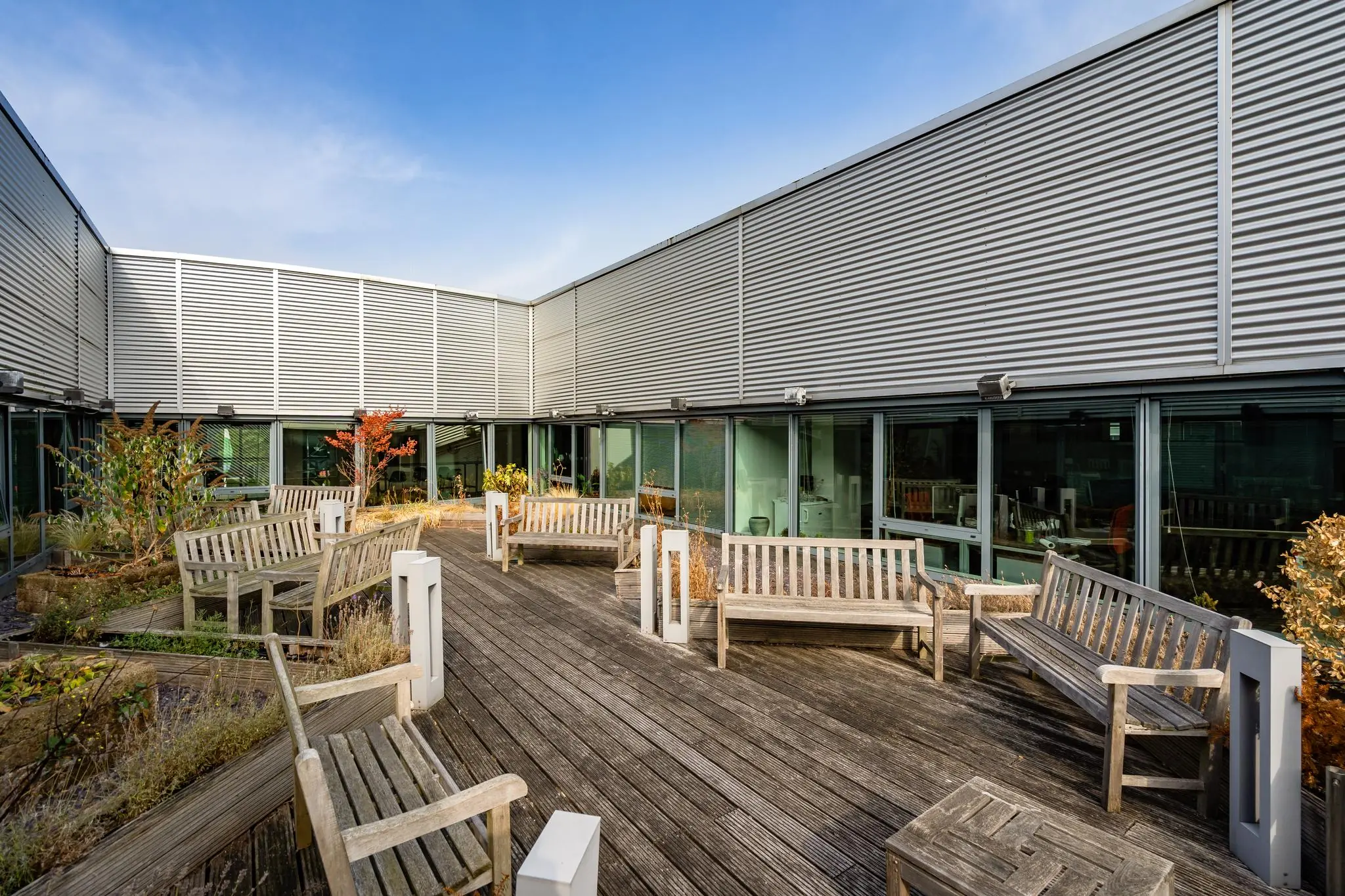 Houten dakterras met bankjes en beplanting op Rivium Boulevard naast een modern kantoorgebouw met glazen gevel.